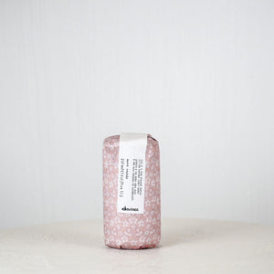 Pink soap bar with a label on a white surface against a light gray background