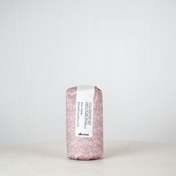 Pink soap bar with a label on a white surface against a light gray background