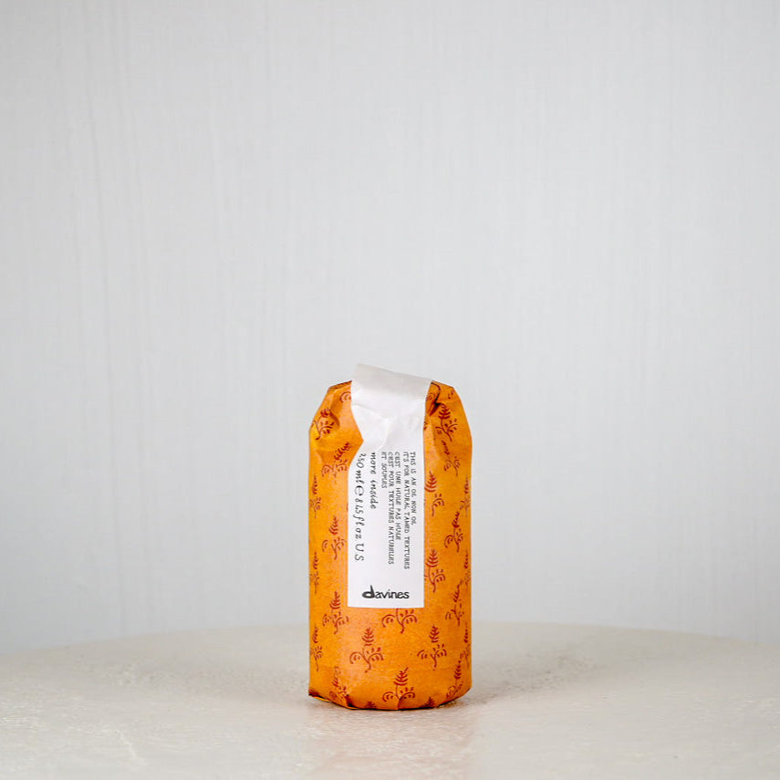 Orange hair product bottle with white label on a light gray background