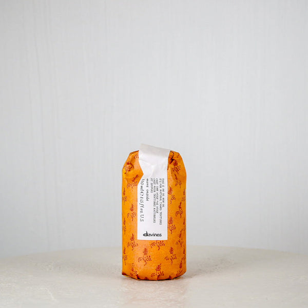 Orange hair product bottle with white label on a light gray background