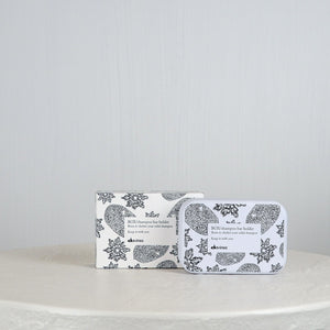 Shampoo bar and holder packaging with floral design on a white surface and light gray background