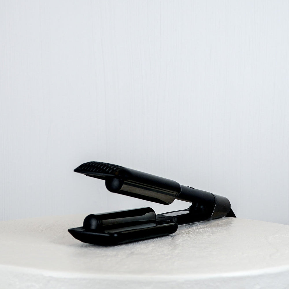 Black hair straightener on a white surface with a light gray background
