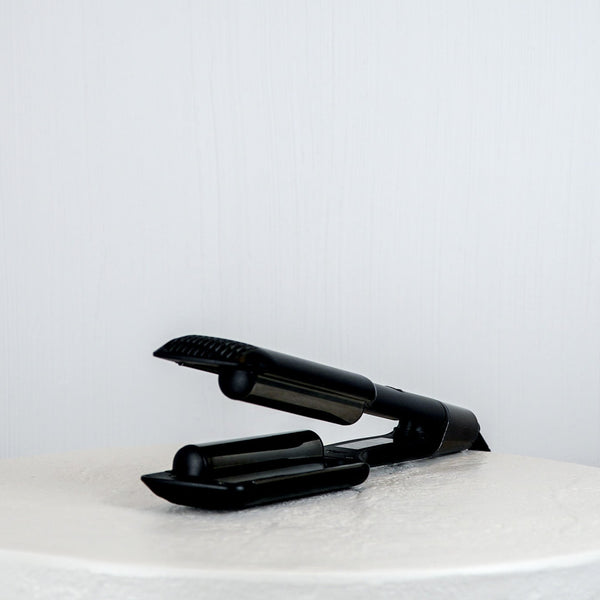 Black hair straightener on a white surface with a light gray background