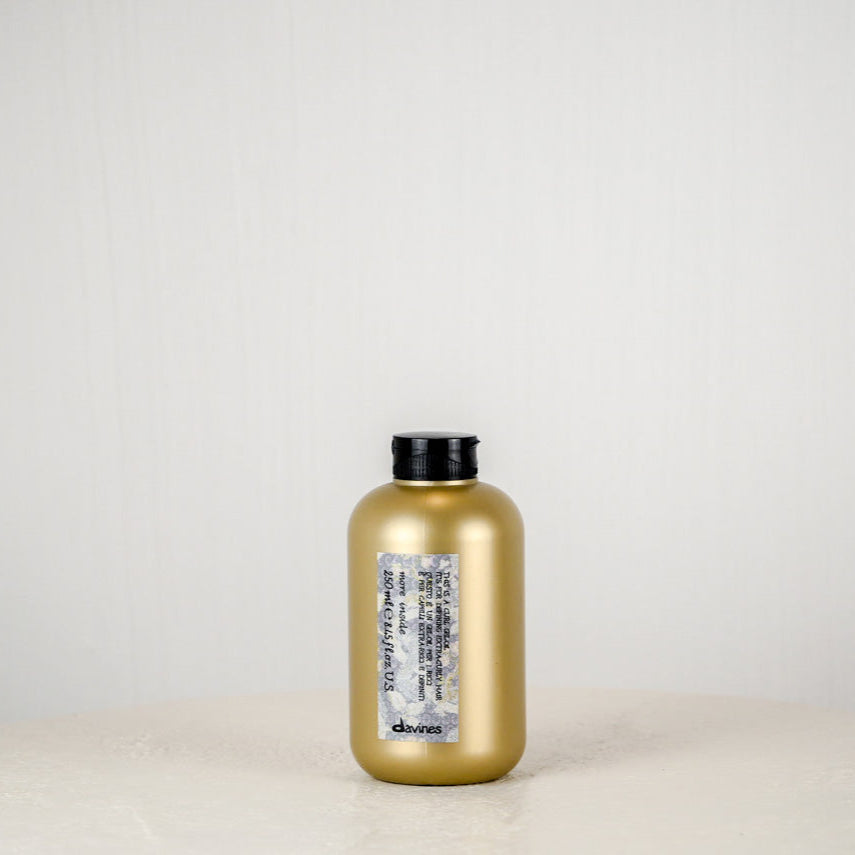 Hair product container with floral design and 'devines' branding on a white background