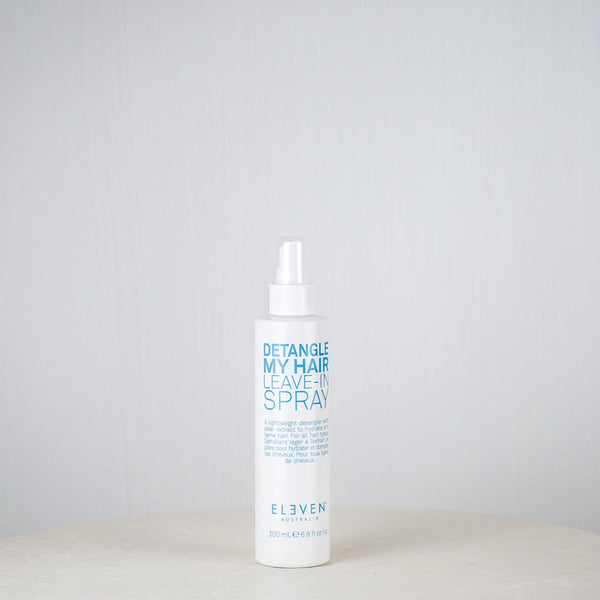 Bottle of 'Eleven' hair care product on a white surface with a gray background
