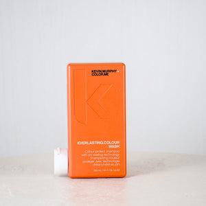 Orange bottle of Kevin Murphy hair product on a white surface with a white background