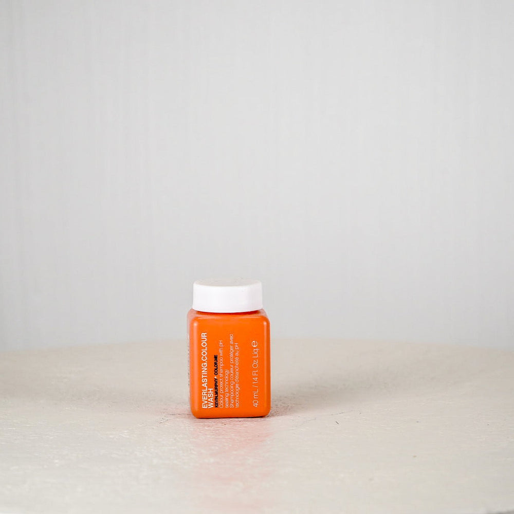 Orange bottle of Kevin Murphy hair product on a white surface with a white background