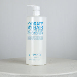 Bottle of 'Hydrate My Hair Moisture Conditioner' by Eleven on a white surface with a gray background
