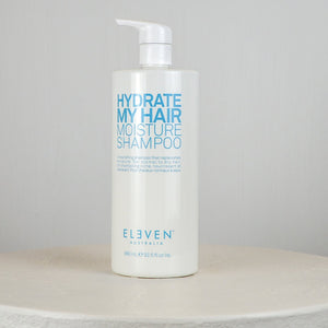 Shampoo bottle labeled 'Hydrate My Hair Moisture Shampoo' by 'Eleven' on a gray background