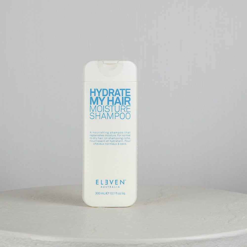 Shampoo bottle labeled 'Hydrate My Hair Moisture Shampoo' by 'Eleven' on a gray background