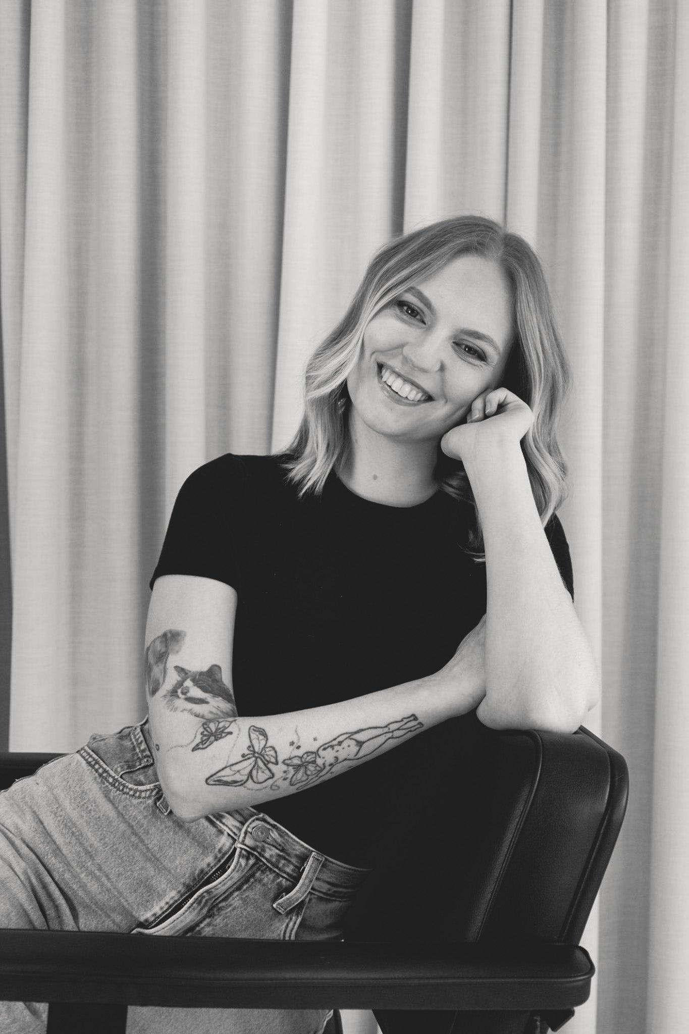 Black and white photo of a person sitting on a chair with a neutral background