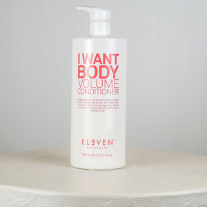 Bottle of 'I Want Body Volume Conditioner' by Eleven on a round stone surface with a light gray background