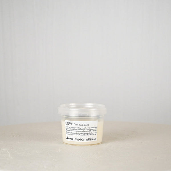 Jar of hair mask on a white surface with a gray background