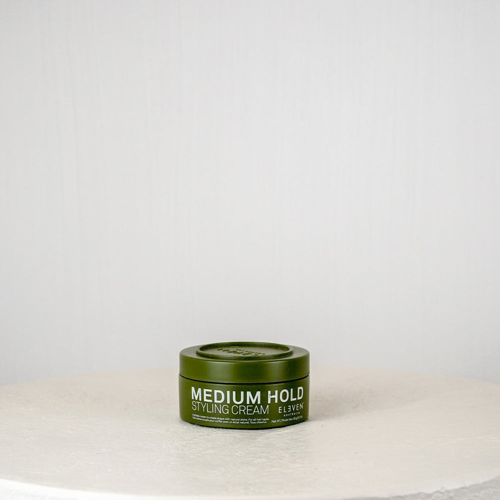 Green hair product container on a white surface with a light gray background