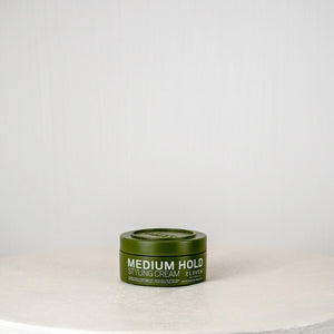 Green hair product container on a white surface with a light gray background