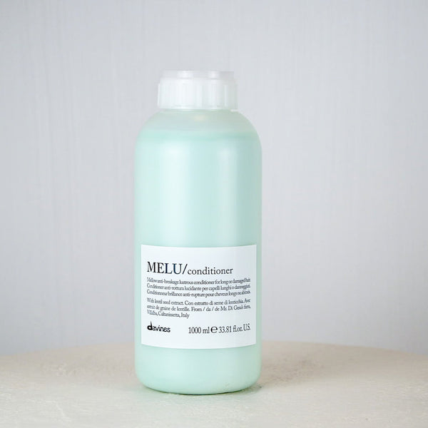 Bottle of Davines MELI conditioner on a white surface with a gray background