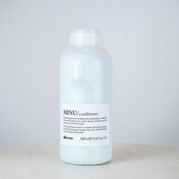 Bottle of Davines MINU conditioner on a white surface with a light gray background