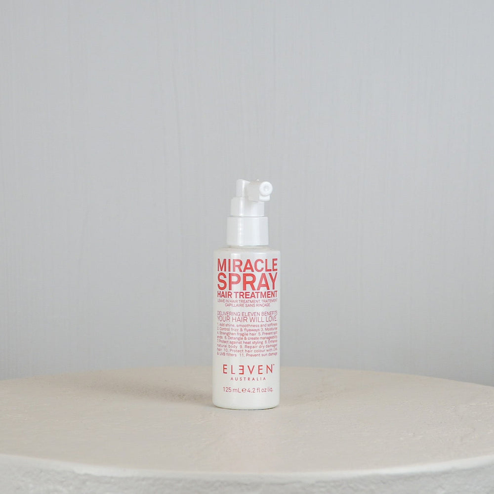 Bottle of 'Miracle Spray' hair treatment on a round white surface with a light gray background