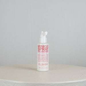 Bottle of 'Miracle Spray' hair treatment on a round white surface with a light gray background