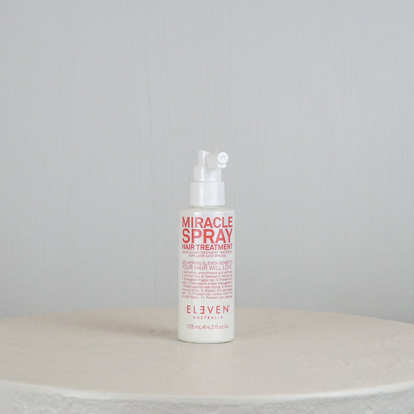 Bottle of 'Miracle Spray' hair treatment on a round white surface with a light gray background