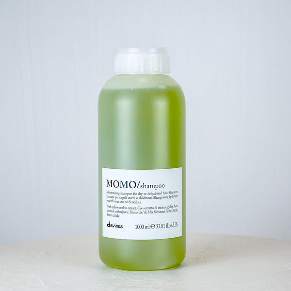 Bottle of green shampoo labeled 'MOMO/shampoo' on a white surface with a light gray background