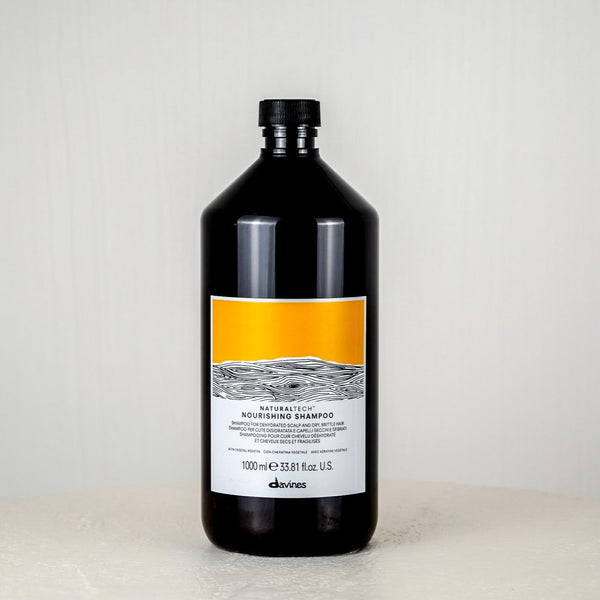 Black shampoo bottle with a label on a white surface and light gray background