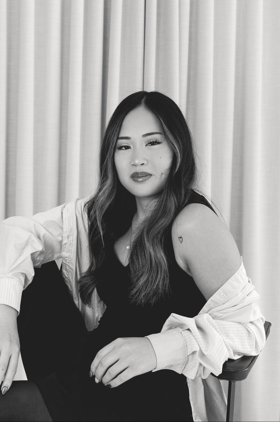Black and white photo of a woman sitting against a curtain backdrop