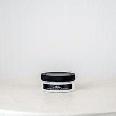 Jar of hair product on a white surface with a light gray background