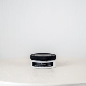 Jar of hair product on a white surface with a light gray background