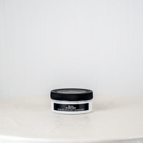 Jar of hair product on a white surface with a light gray background
