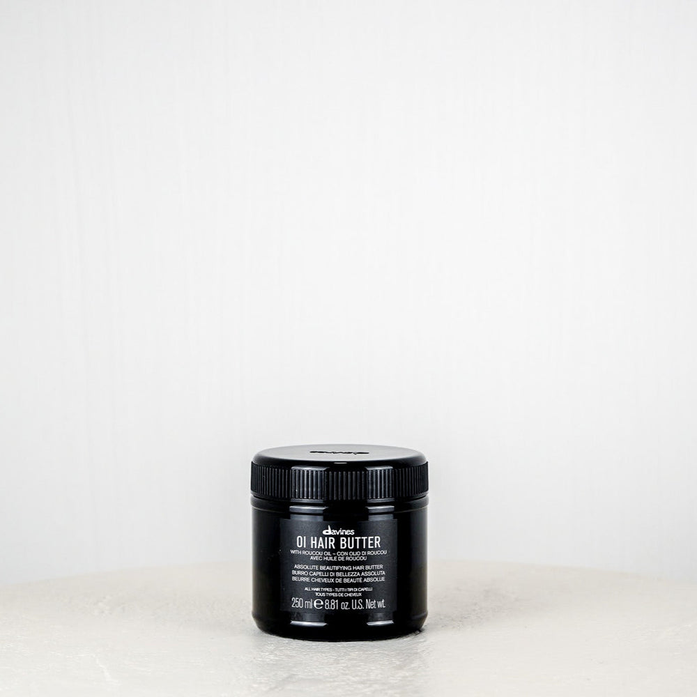 Black jar of hair butter on a white surface with a white background