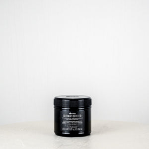 Black jar of hair butter on a white surface with a white background