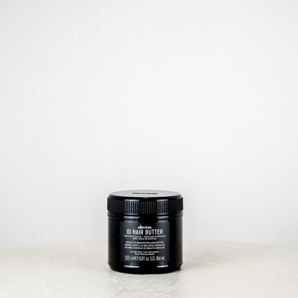 Black jar of hair butter on a white surface with a white background