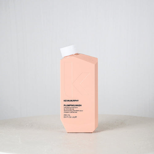 Pink bottle of Kevin Murphy Plumping Wash on a white surface with a light gray background