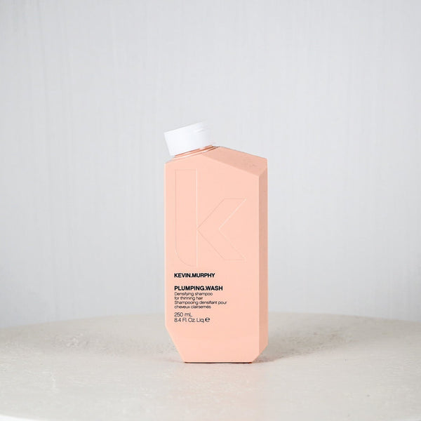 Pink bottle of Kevin Murphy Plumping Wash on a white surface with a light gray background