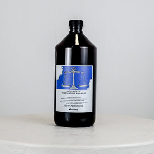 Black shampoo bottle with a label on a white surface against a gray background