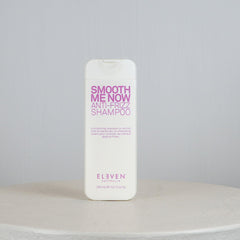 Shampoo bottle labeled 'Smooth Me Now Anti-Frizz Shampoo' by 'Eleven' on a gray background