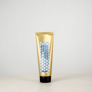 Gold tube of hair product on a white surface with a light gray background