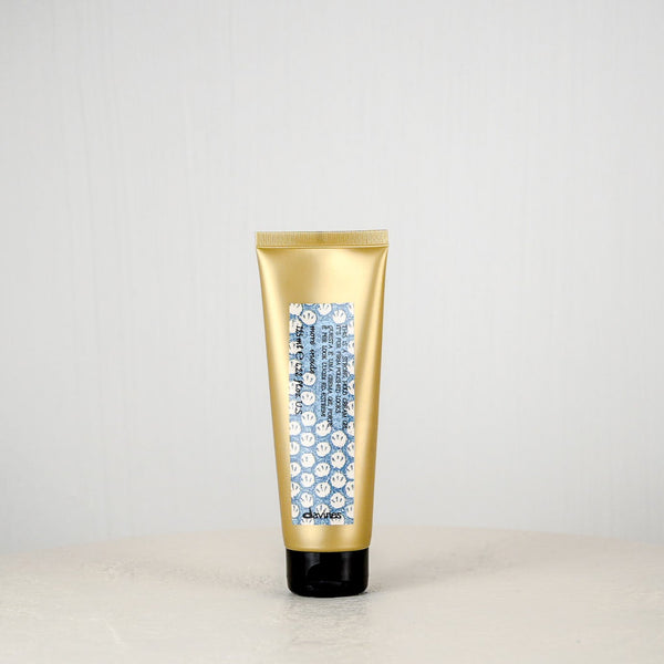 Gold tube of hair product on a white surface with a light gray background